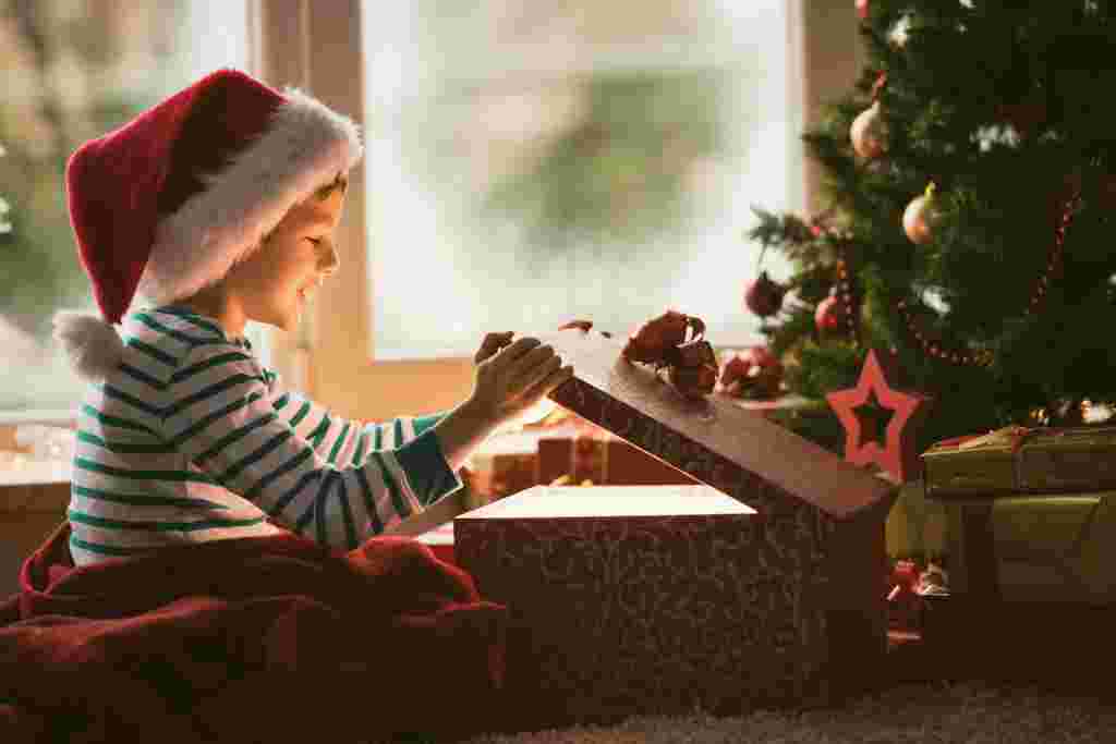 Little boy opening Christmas present, smiling and looking at shiny box.